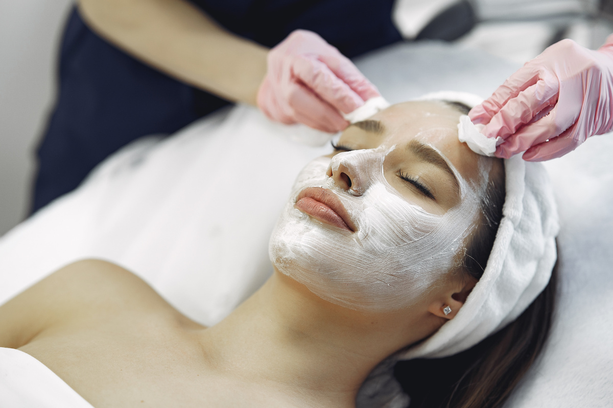 Crop woman in medical gloves removing cosmetic mask from face of female client in spa salon